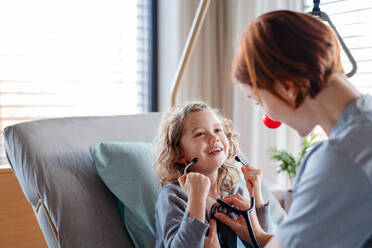 Friendly female doctor with stethoscope examining small girl in bed in hospital. - HPIF13051