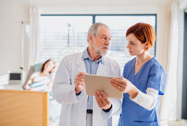 Vorderansicht eines Arztes und einer Krankenschwester mit einem Tablet, die in einem Krankenhauszimmer Probleme besprechen. - HPIF13066