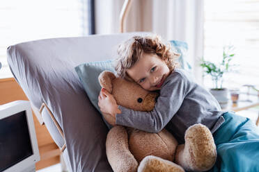 Lächelndes kleines Mädchen mit Teddybär im Bett im Krankenhaus, das in die Kamera schaut. - HPIF13081