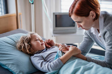 Eine fürsorgliche Mutter besucht ihre kleine Tochter im Krankenhaus und streichelt ihr Gesicht. - HPIF13093