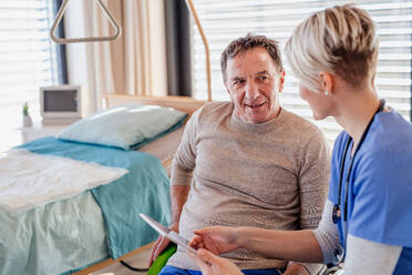 A healthcare worker with tablet and senior patient in wheelchair in hospital or at home, talking. - HPIF13101