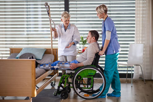 Frauen im Gesundheitswesen und ein älterer Patient im Rollstuhl im Krankenhaus im Gespräch. - HPIF13114