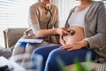 Eine nicht erkennbare medizinische Fachkraft untersucht eine schwangere Frau zu Hause. - HPIF13120