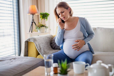 A portrait of pregnant woman in pain indoors at home, making emergency call. - HPIF13127