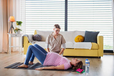 Physiotherapeutin und schwangere Frau bei Übungen auf dem Boden zu Hause. - HPIF13129