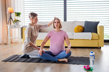 Zufriedene schwangere Frau bei einer Yoga-Übung mit Lehrer zu Hause. - HPIF13130
