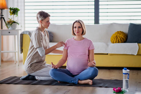 Zufriedene schwangere Frau bei einer Yoga-Übung mit Lehrer zu Hause. - HPIF13131