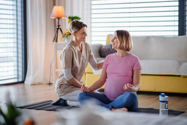 Mitarbeiterin des Gesundheitswesens und aktive schwangere Frau zu Hause bei einer Yogaübung. - HPIF13132