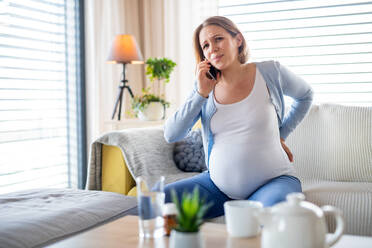 A portrait of pregnant woman in pain indoors at home, making phone call. - HPIF13134