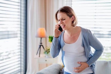 A portrait of pregnant woman in pain indoors at home, making emergency call. - HPIF13135