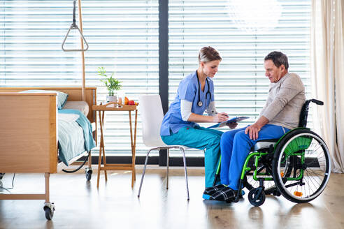 Eine Pflegekraft und ein älterer Patient im Rollstuhl im Krankenhaus oder zu Hause im Gespräch. - HPIF13163