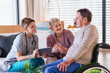 A healthcare worker with tablet visiting senior patient in wheelchair at home, talking. - HPIF13165