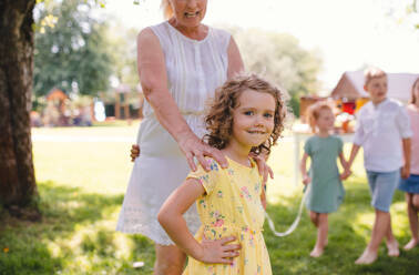 Small children with grandmother outdoors in garden in summer, playing. - HPIF13172