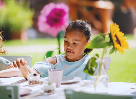 Kleines Mädchen, das im Sommer im Garten sitzt und Snacks isst - ein Konzept für eine Feier. - HPIF13177
