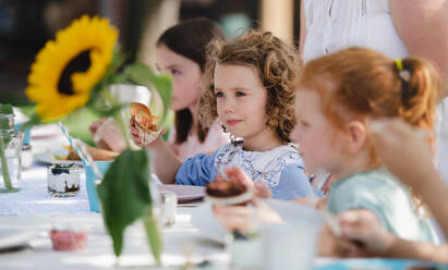 Happy small girls sitting and eating at table on summer garden party, birthday celebration concept. - HPIF13186