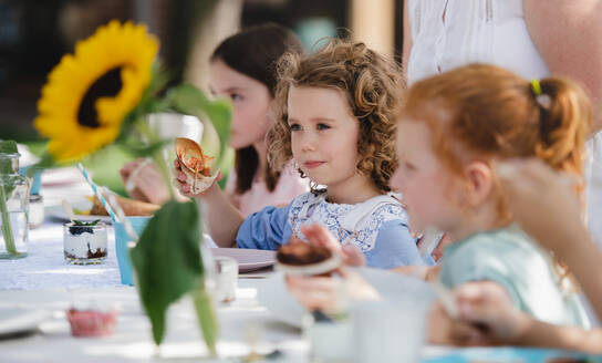 Glückliche kleine Mädchen sitzen und essen am Tisch auf Sommergarten Party, Geburtstagsfeier Konzept. - HPIF13186