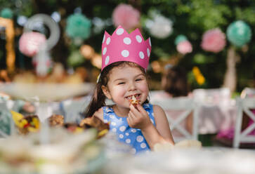 Freches kleines Mädchen, das im Sommer im Garten sitzt und Snacks isst, ein Konzept zum Feiern. - HPIF13189