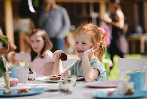 Glückliche kleine Mädchen sitzen und essen am Tisch auf Sommergarten Party, Geburtstagsfeier Konzept. - HPIF13190