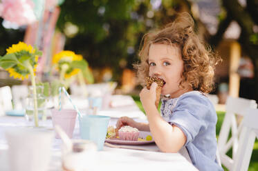 Kleines Mädchen, das im Sommer im Garten sitzt und Snacks isst - ein Konzept für eine Feier. - HPIF13192