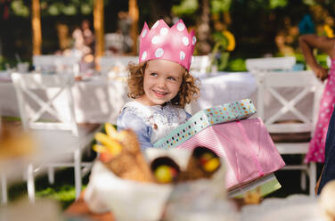 Kleines Mädchen mit Hut im Garten im Sommer, mit Geschenken in der Hand, ein Festkonzept. - HPIF13194