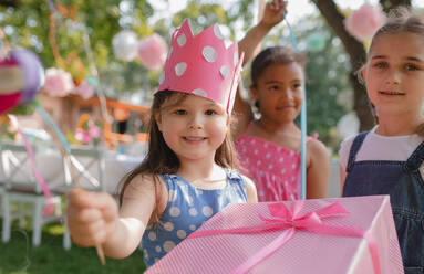 A portrait of small girl with friends and present outdoors in garden in summer. - HPIF13201