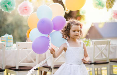 Porträt eines glücklichen kleinen Mädchens, das mit Luftballons im Freien auf einer Gartenparty im Sommer spielt. - HPIF13205