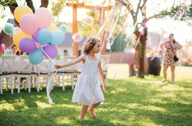 Porträt eines glücklichen kleinen Mädchens, das mit Luftballons im Freien auf einer Gartenparty im Sommer spielt. - HPIF13206