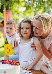 Front view of small girl with cake and grandmother celebrating birthday outdoors in garden in summer, party concept. - HPIF13208