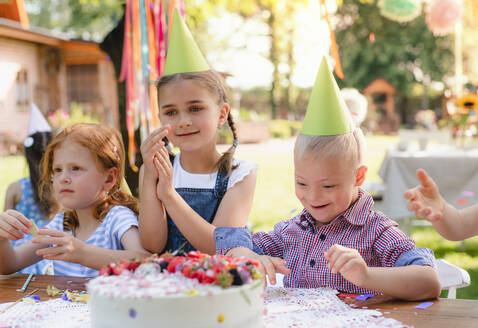 Down-Syndrom-Kind mit Freunden auf Geburtstagsfeier im Freien im Garten im Sommer. - HPIF13215