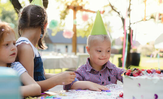 Down-Syndrom-Kind mit Freunden auf Geburtstagsfeier im Freien im Garten im Sommer. - HPIF13216