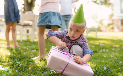 Down-Syndrom-Kind mit Freunden auf Geburtstagsparty im Freien im Garten im Sommer, öffnen Geschenke. - HPIF13218