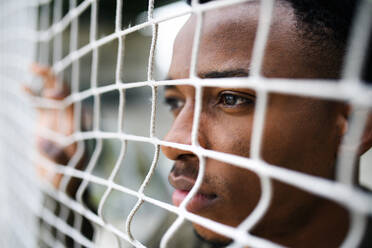 Frustrated young black man behind net outdoors in city, black lives matter and discrimination concept. - HPIF13254