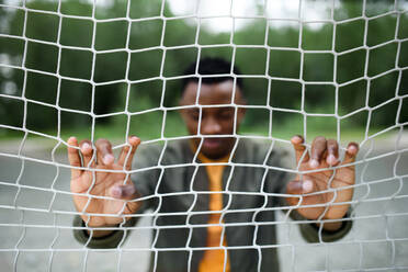 Frustrated young black man behind net outdoors in city, black lives matter and discrimination concept. - HPIF13255