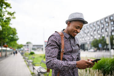 Cheerful young black man commuter with smartphone outdoors in city, walking. - HPIF13288