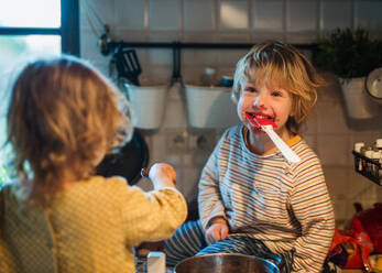 Glücklicher kleiner Junge und Mädchen drinnen in der Küche zu Hause, die beim Kochen helfen. - HPIF13296