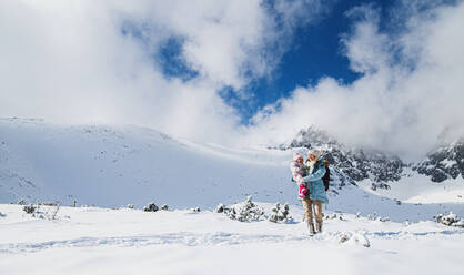 Portrait of mother with happy small daughter standing in winter nature, walking. - HPIF13298