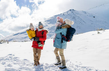 Frontalaufnahme von Vater und Mutter mit zwei kleinen Kindern in winterlicher Natur, stehend im Schnee. - HPIF13299