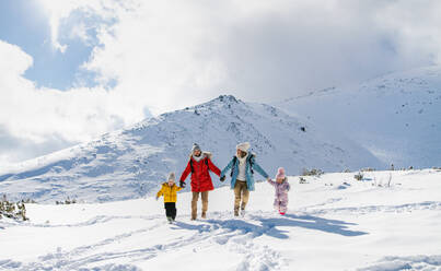 Frontalaufnahme von Vater und Mutter mit zwei kleinen Kindern in winterlicher Natur, die im Schnee spazieren gehen. - HPIF13301