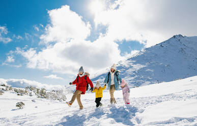 Porträt von Vater und Mutter mit zwei kleinen Kindern in winterlicher Natur, die im Schnee spazieren gehen. - HPIF13306