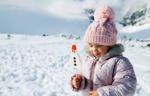 Porträt eines fröhlichen kleinen Mädchens im Schnee in der winterlichen Natur, das einen Schneemann-Lutscher hält. Kopierraum. - HPIF13307