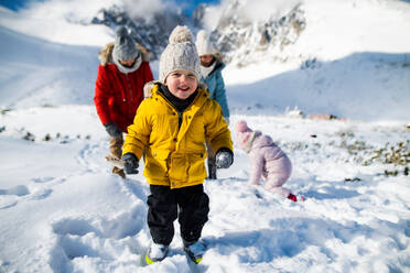 Kleiner Junge mit Familie in winterlicher Natur, der im Schnee spazieren geht und in die Kamera schaut. - HPIF13322