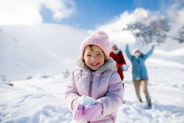 Porträt eines fröhlichen kleinen Mädchens, das im Schnee in der winterlichen Natur spielt und in die Kamera schaut. - HPIF13324