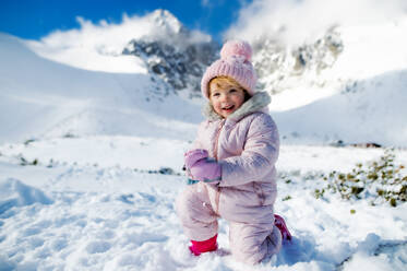 Porträt eines fröhlichen kleinen Mädchens, das im Schnee in der winterlichen Natur liegt, spielt und in die Kamera schaut. - HPIF13325