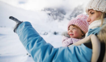 Junge Mutter mit kleiner Tochter im Kinderwagen in winterlicher Natur stehend, im Gespräch. - HPIF13329