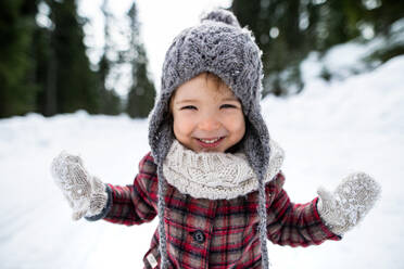 Front view portrait of cheerful small toddler girl standing in winter nature, looking at camera. - HPIF13345