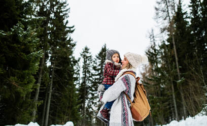 Seitenansicht einer fröhlichen Mutter mit kleiner Tochter in winterlicher Natur. - HPIF13358