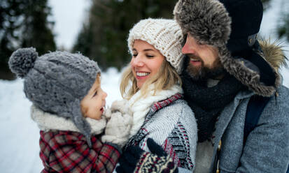 Seitenansicht von Vater und Mutter mit Kleinkind in winterlicher Natur, stehend im Schnee. - HPIF13359