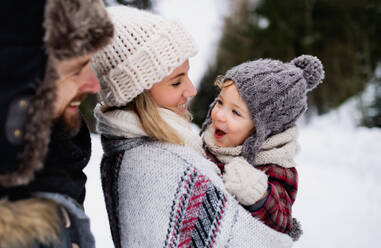Seitenansicht von Vater und Mutter mit Kleinkind in winterlicher Natur, stehend im Schnee. - HPIF13360