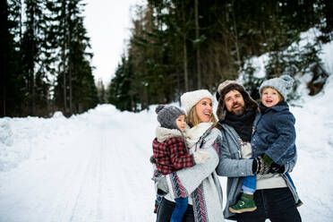 Seitenansicht Porträt von Vater und Mutter mit zwei kleinen Kindern in winterlicher Natur, stehend im Schnee. - HPIF13362