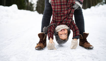 Mittelteil einer nicht erkennbaren Mutter, die ihre kleine Tochter in der winterlichen Natur auf dem Kopf hält. - HPIF13364